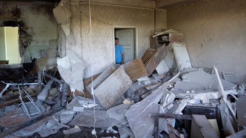 Blick in das zerstörte Zimmer voller Schutt. Ein Mann steht in einem Türrahmen und schaut auf die Zerstörung.