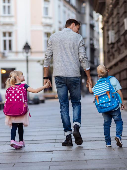 Rückansicht von zwei Kindern auf dem Weg zur Schule mit einer älteren Person