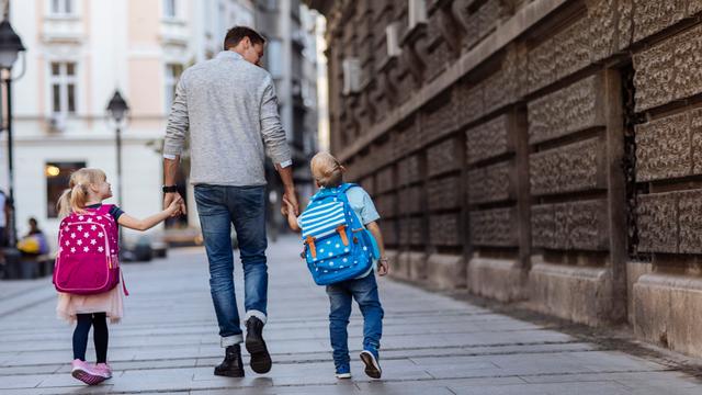 Rückansicht von zwei Kindern auf dem Weg zur Schule mit einer älteren Person