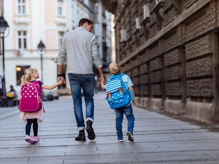 Rückansicht von zwei Kindern auf dem Weg zur Schule mit einer älteren Person