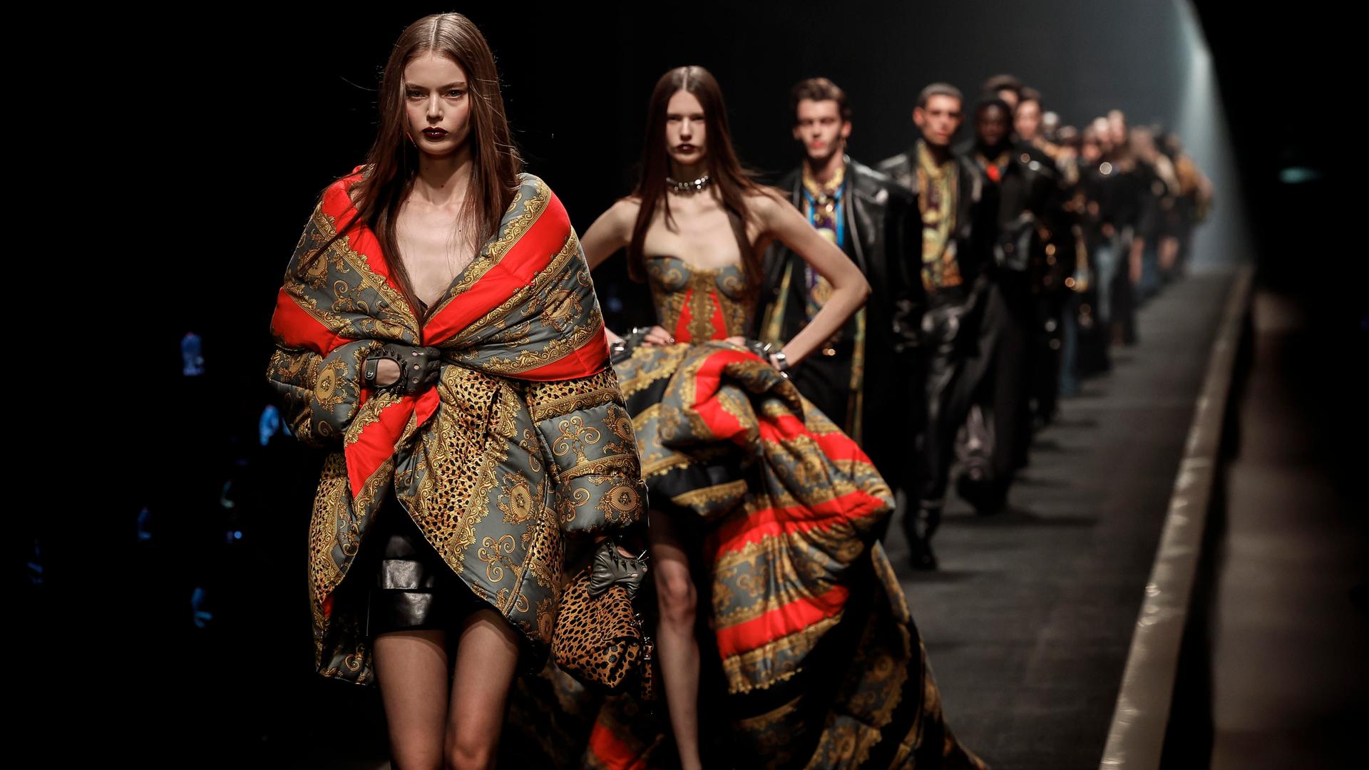 Weibliche und männliche Models gehen für Versace hintereinander über den Laufsteg.