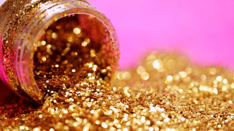 Goldener Glitzer läuft aus einem kleinen Glasbehälter.