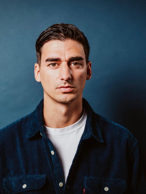 Portraitaufnahme von Cihan Acar im petrolfarbenen Cordhemd vor petrolfarbenem Hintergrund.