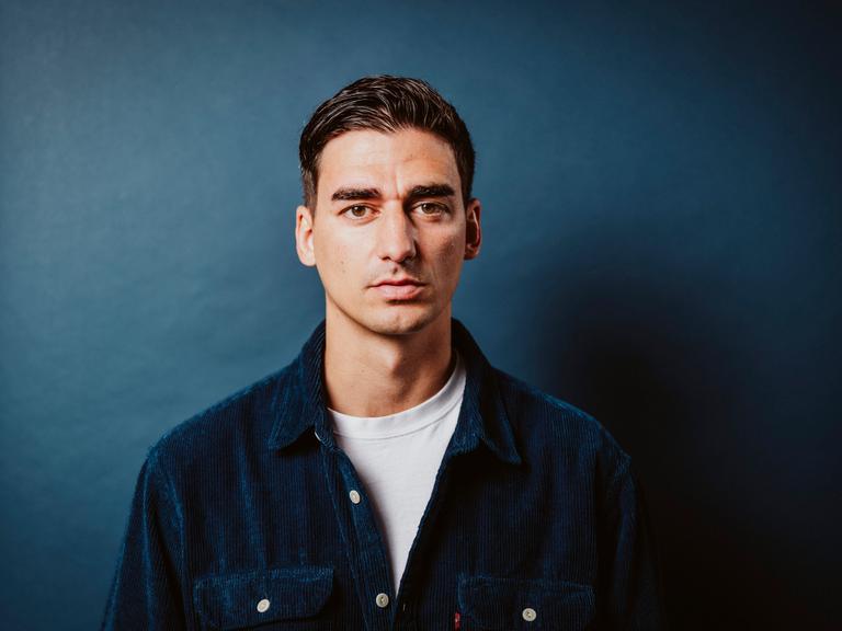 Portraitaufnahme von Cihan Acar im petrolfarbenen Cordhemd vor petrolfarbenem Hintergrund.