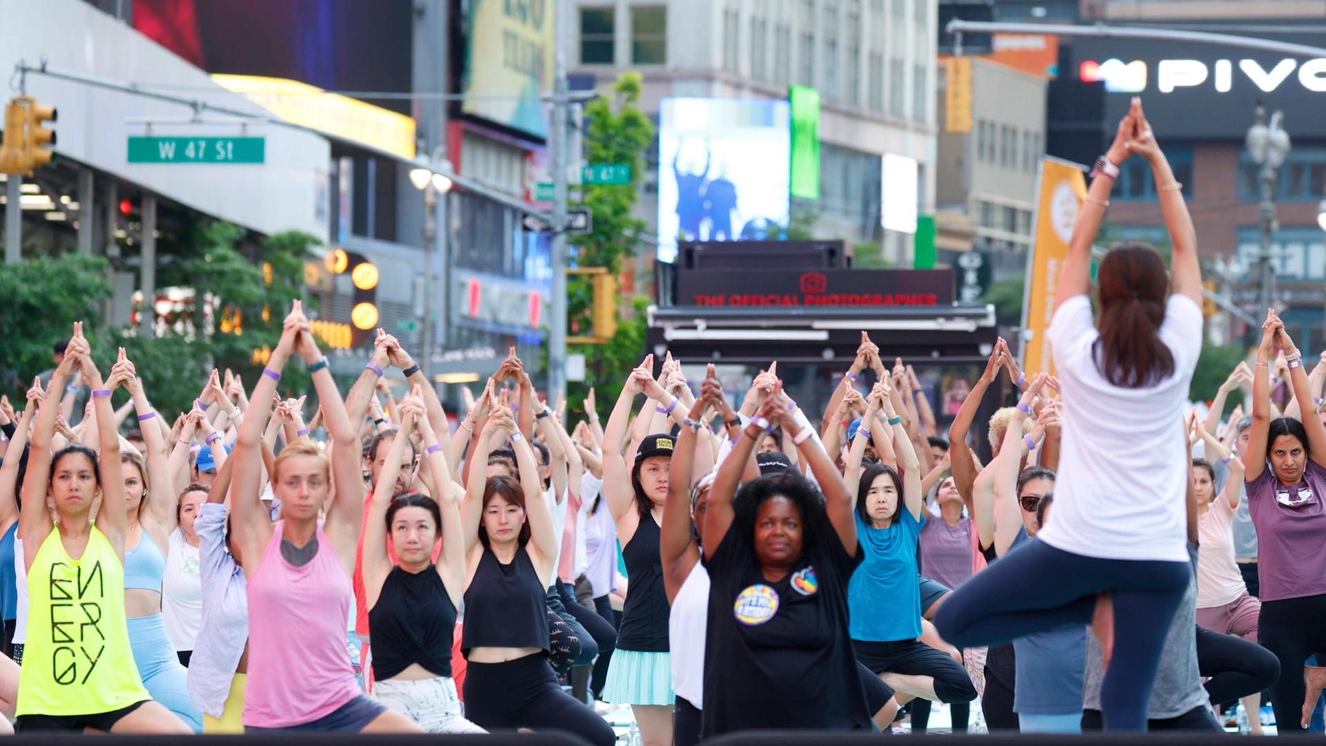 Menschen stehen nebeneinander auf dem Time Square in New York und machen eine Yogaübung: Yogastunde zur Feier der Sommersonnenwende