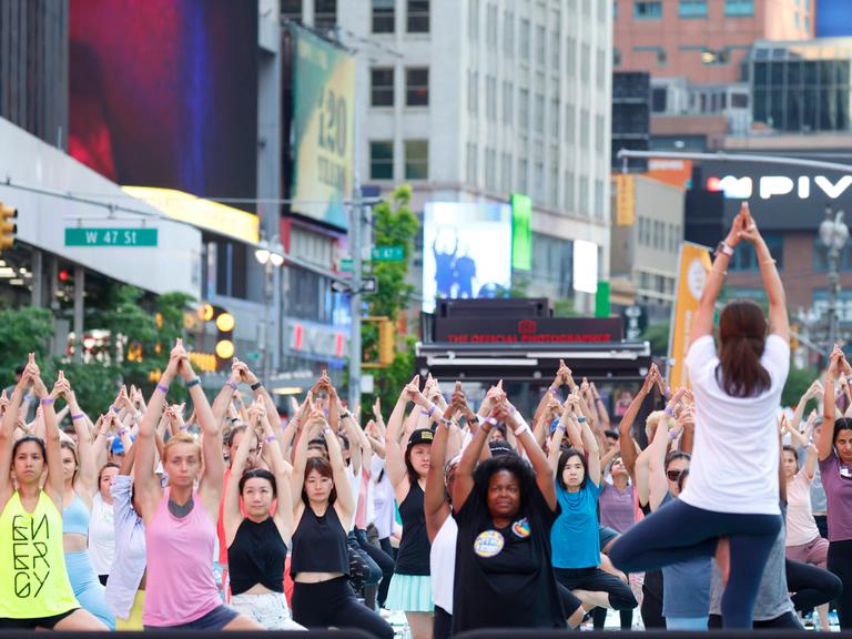 Menschen stehen nebeneinander auf dem Time Square in New York und machen eine Yogaübung: Yogastunde zur Feier der Sommersonnenwende
