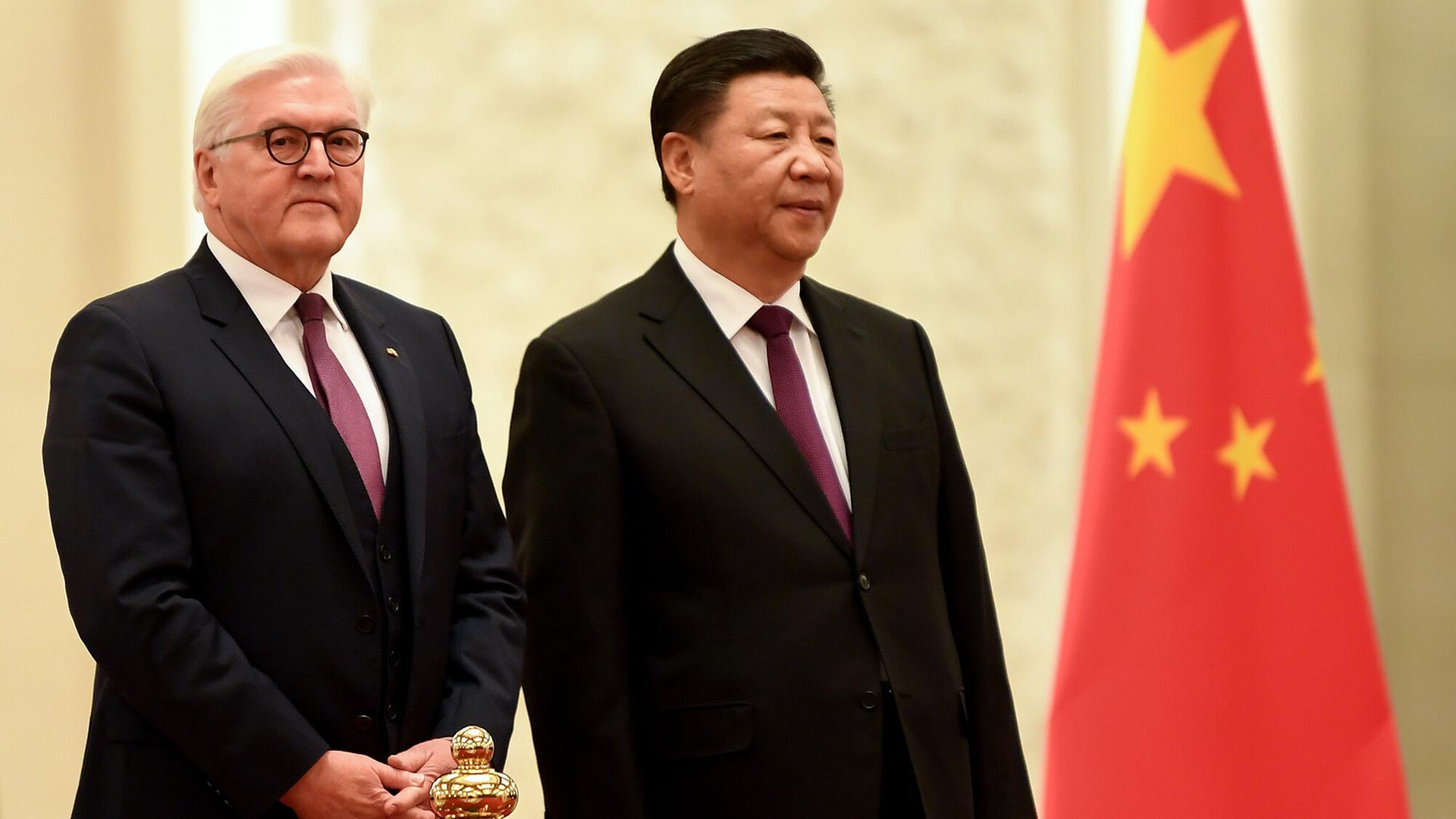 Bundespräsident Steinmeier und der chinesische Präsident Xi Jinping stehen nebeneinander. Neben ihnen ist die chinesische Flagge zu sehen. 