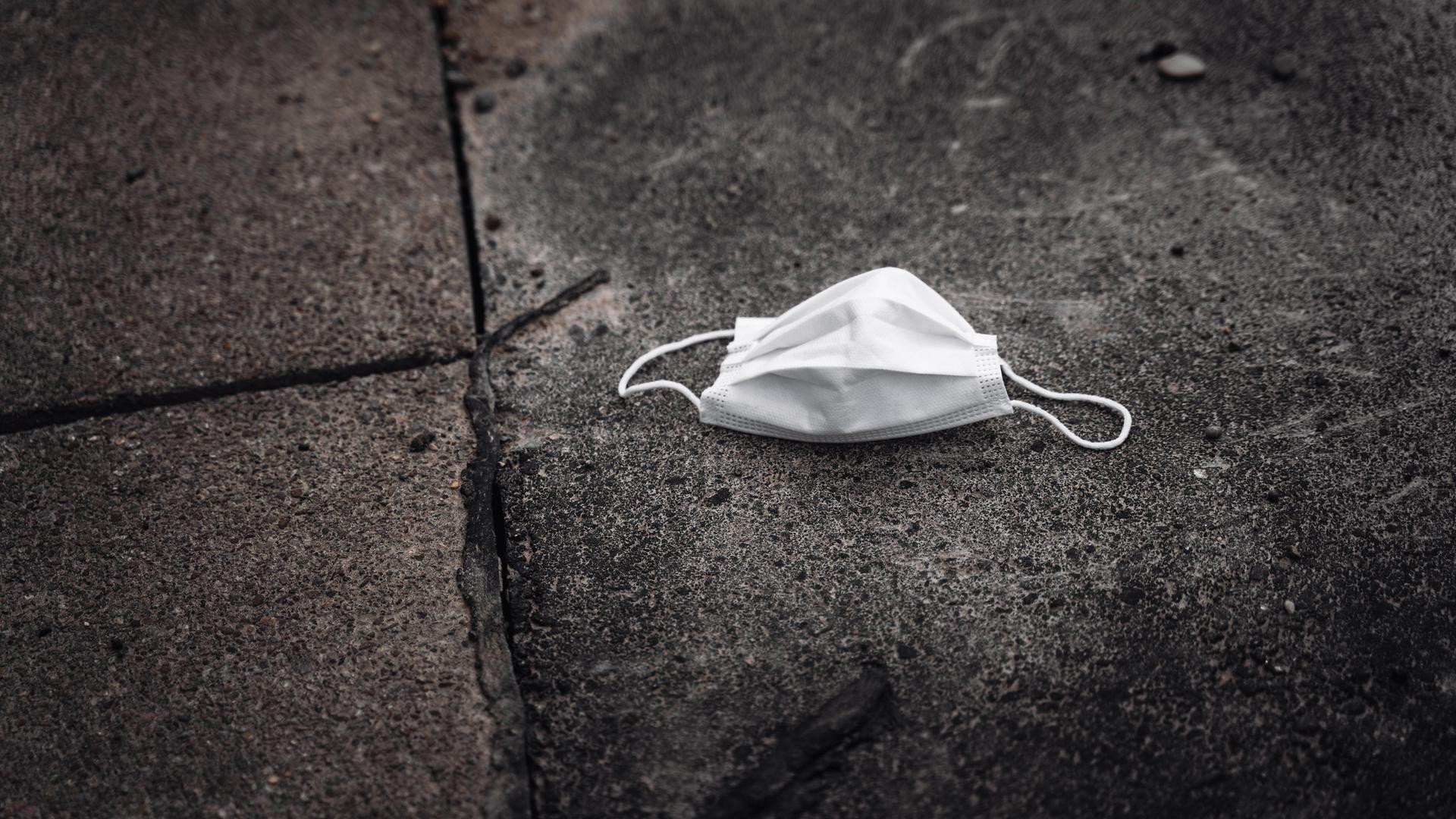 Ein weiße gebrauchte medizinische Maske liegt auf dem schmutzigen Boden. 