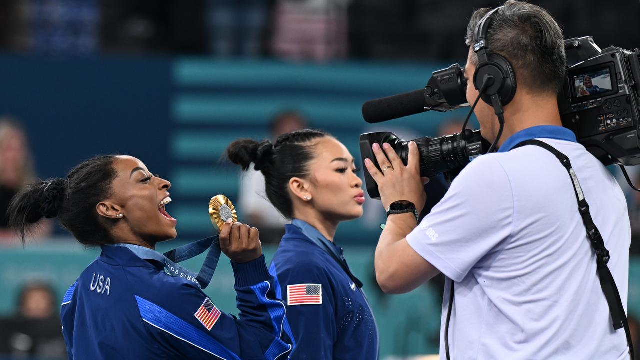 Olympia, Paris 2024, Turnen, Mehrkampf, Frauen, Finale, Simone Biles (l) aus den USA jubelt mit ihrer Goldmedaille vor einer TV-Kamera.