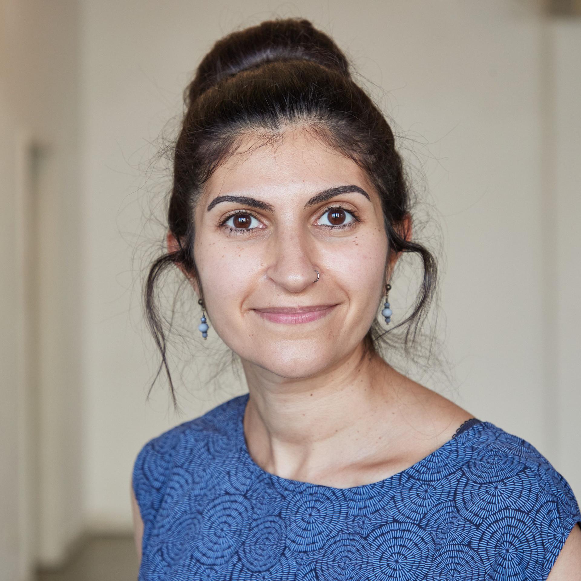 Shida Bazyar schaut in die Kamera. Sie hat ihre schwarzen Haare hochgesteckt, ihr Kleid ist blau-schwarz gemustert.