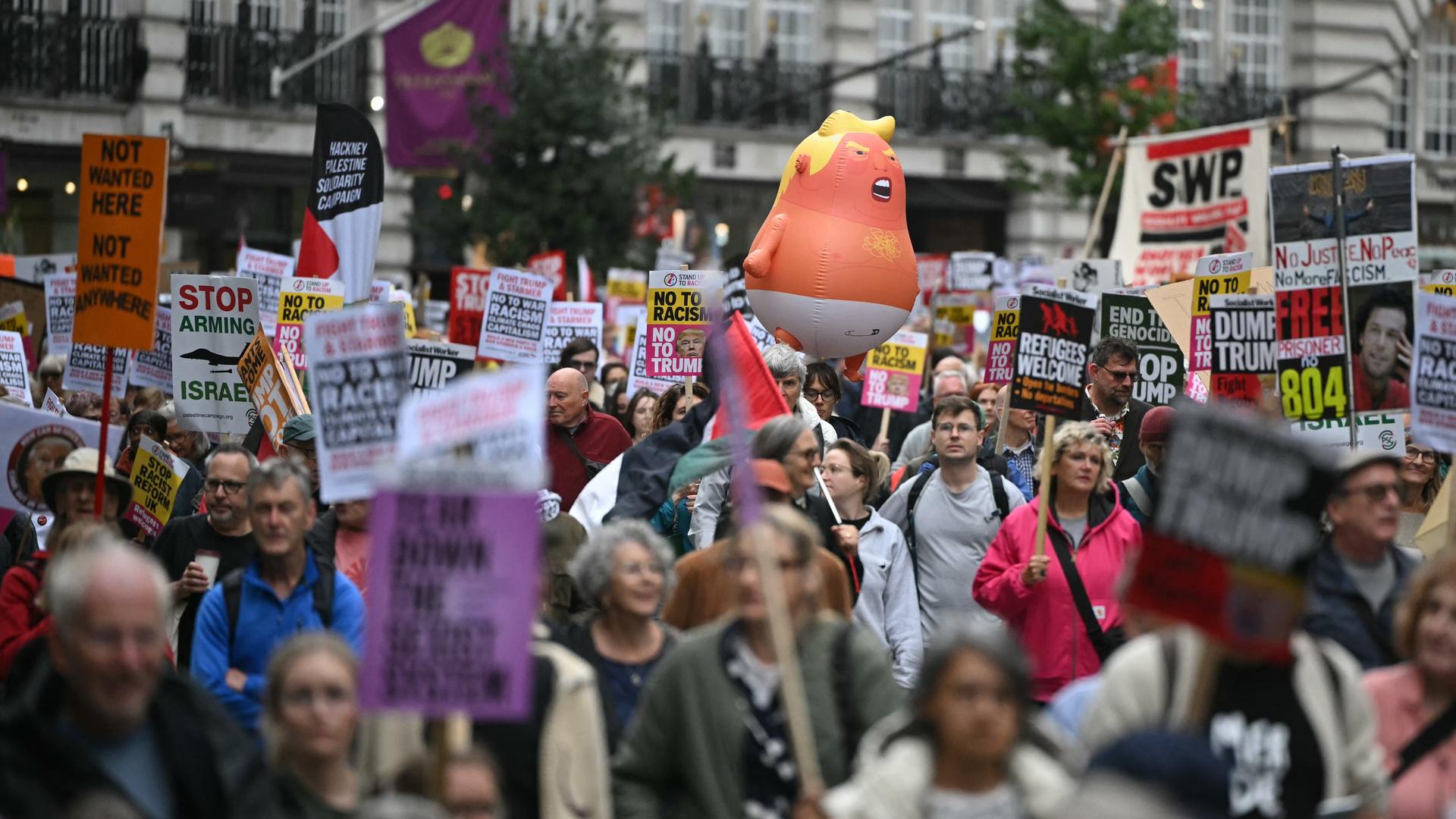 Viele Menschen laufen über eine Straße und halten Protestschilder hoch. Viele Menschen laufen über eine Straße und halten Protestschilder hoch.