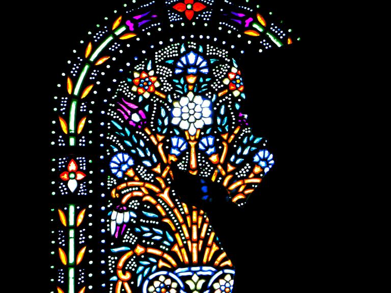 Vor einem leuchtend strahlendem Kirchenfenster zeichnen sich die Umrisse einer dankenden Frau ab.