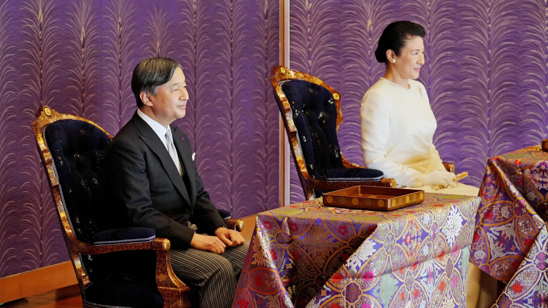 Der japanische Kaiser Naruhito und die Kaiserin Masako sitzen vor geschmückten Tischen.