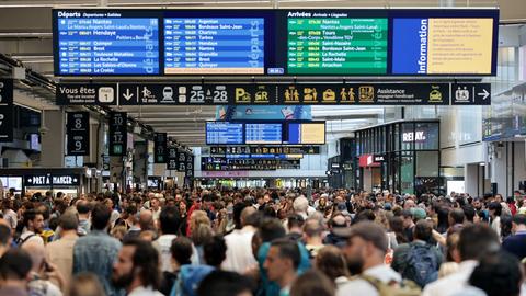 Fahrgäste stehen in der Bahnstation Montparmasse in Paris und schauen auf Anzeigetafeln.