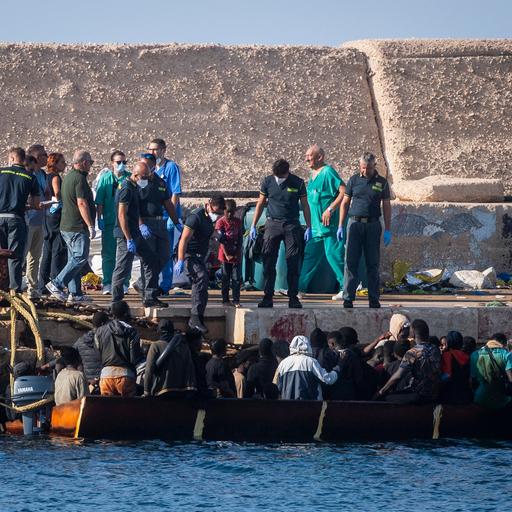 Viele Menschen auf einem Boot kommen an einem Hafen in Italien an. Helfer an Land strecken ihnen die Hand entgegen.
