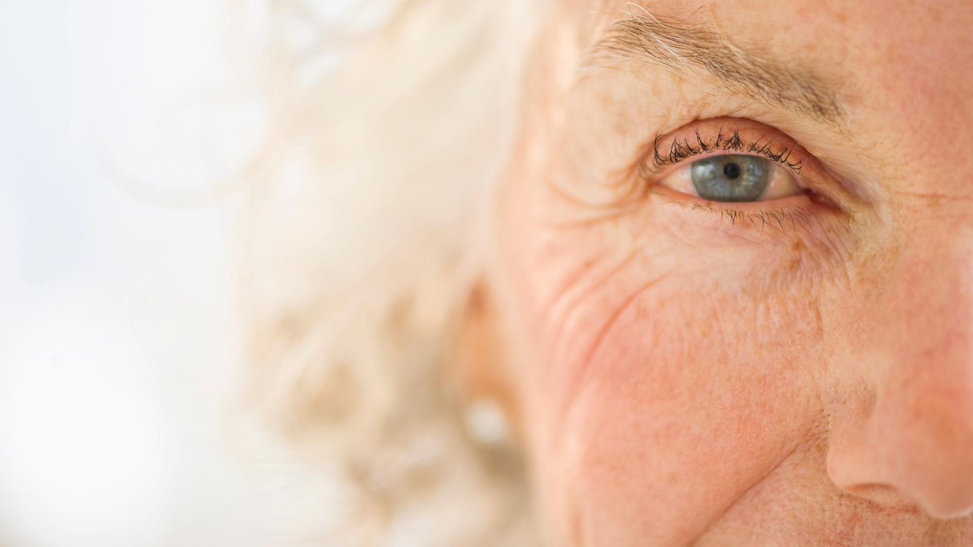 Nahaufnahme vom Gesicht einer älteren Frau. Zu sehen ist ein Auge und die Nase im Anschnitt. Im Hintergrund verwischt ihr graues Haar in der Unschärfe.