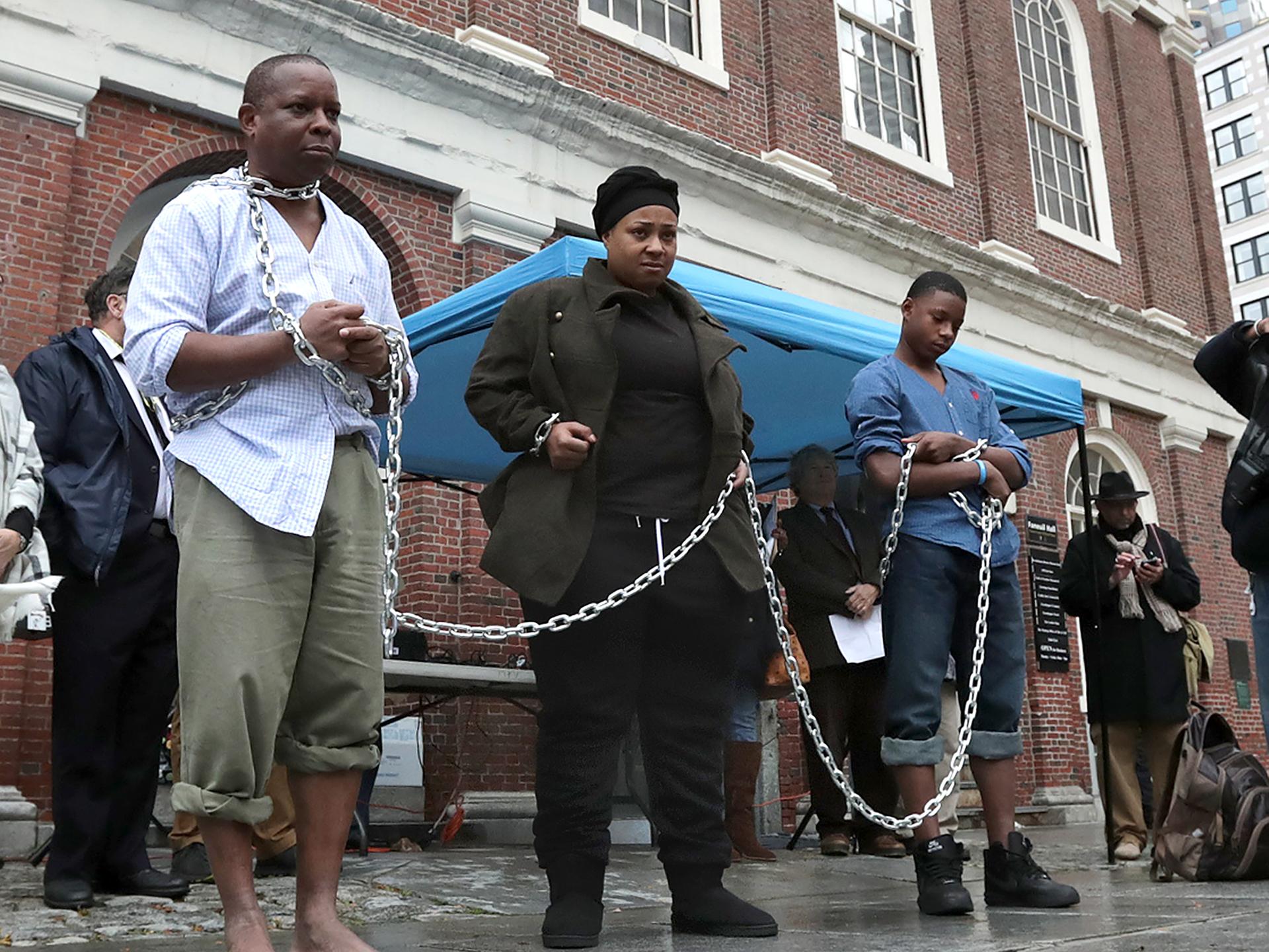 Eine Gruppe von PoC stehen mit Ketten nebeneinander gereiht vor einem Gebäude in Boston.