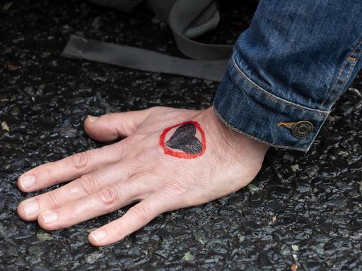 Eine auf dem Asphalt einer Straße festgeklebte Hand.