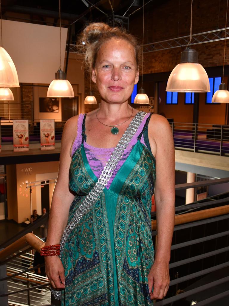Amrei Bauer steht in einem Raum mit großen Lampenschirmen im Hintergrund. Sie trägt ein grünes Kleid und schaut fröhlich in die Kamera.
