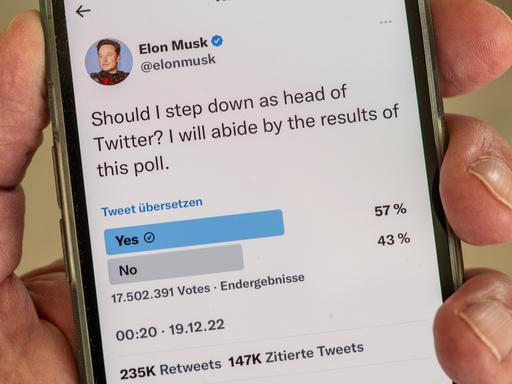 Eine Hand hält ein Smartphone, darauf zu sehen der Tweet von Elon Musk, der fragt, ob er als Twitter-Chef zurücktreten soll.