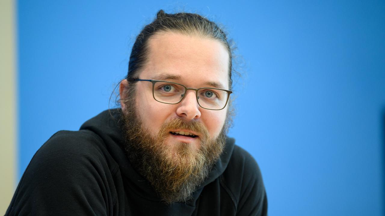 Arne Semsrott, Projektleiter von FragDenStaat, mit Bart, Dutt und Brille vor blauen Hintergrund.