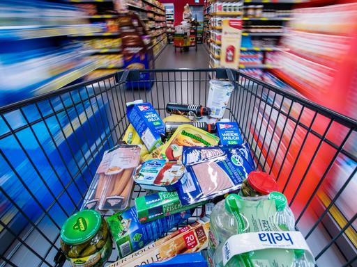 Ein Einkaufswagen mit Lebensmitteln wird am 30.11.2017 in Schwerin (Mecklenburg-Vorpommern) durch die Regalreihen in einem Supermarkt geschoben. Es gibt einen zentralen Fluchtpunkt, die Regale links und rechts sind unscharf, wie bei hoher Geschwindigkeit.