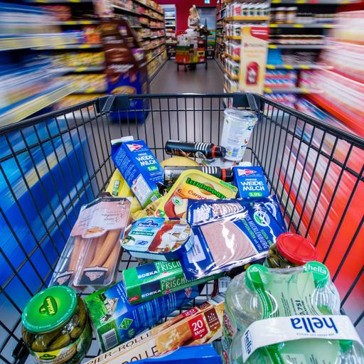 Ein Einkaufswagen mit Lebensmitteln wird am 30.11.2017 in Schwerin (Mecklenburg-Vorpommern) durch die Regalreihen in einem Supermarkt geschoben. Es gibt einen zentralen Fluchtpunkt, die Regale links und rechts sind unscharf, wie bei hoher Geschwindigkeit.