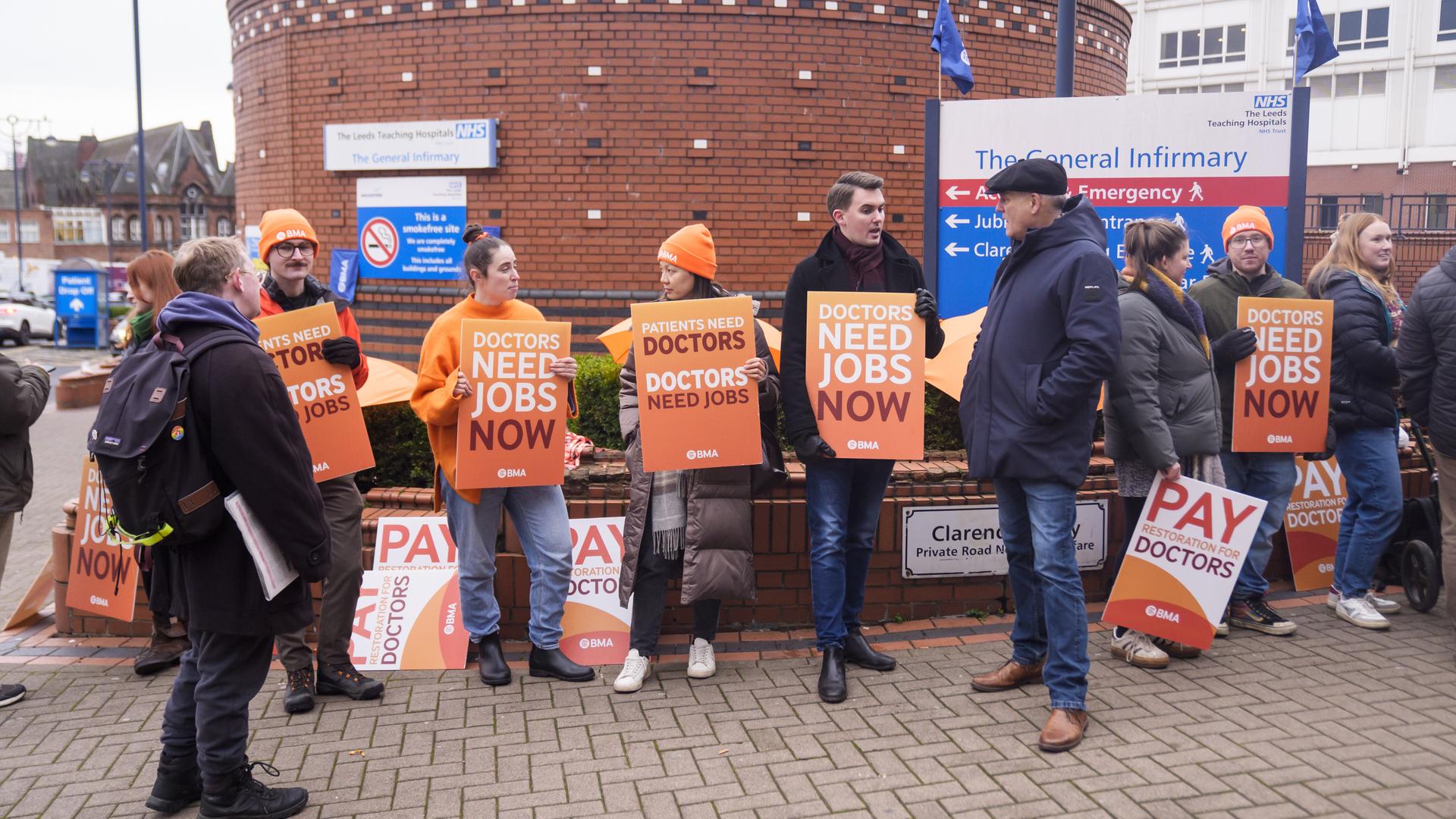 Assistenzärzte stehen mit Plakaten vor einem Steinturm auf einem Platz außerhalb der Leeds General Infirmary.