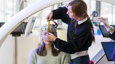 Eine Person bringt auf dem Kopf einer anderen Person ein Brain-Computer-Interface an. Das Cottbuser Startup Zander Laboratories forscht und entwickelt solche Geräte.