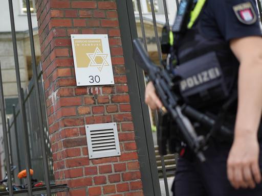 Eine Polizistin steht am Eingang der Jüdischen Gemeinde an der Talmud-Thora-Schule. Eine Hand hat sie an einem Maschinengewehr, das sie vor sich trägt.