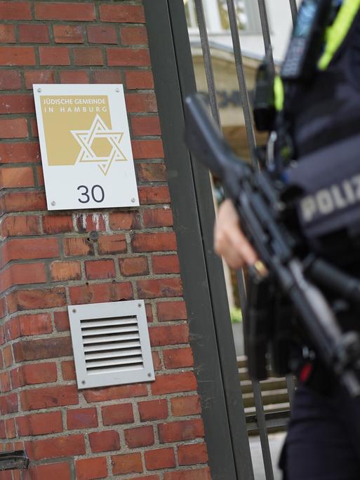 Eine Polizistin steht am Eingang der Jüdischen Gemeinde an der Talmud-Thora-Schule. Eine Hand hat sie an einem Maschinengewehr, das sie vor sich trägt.