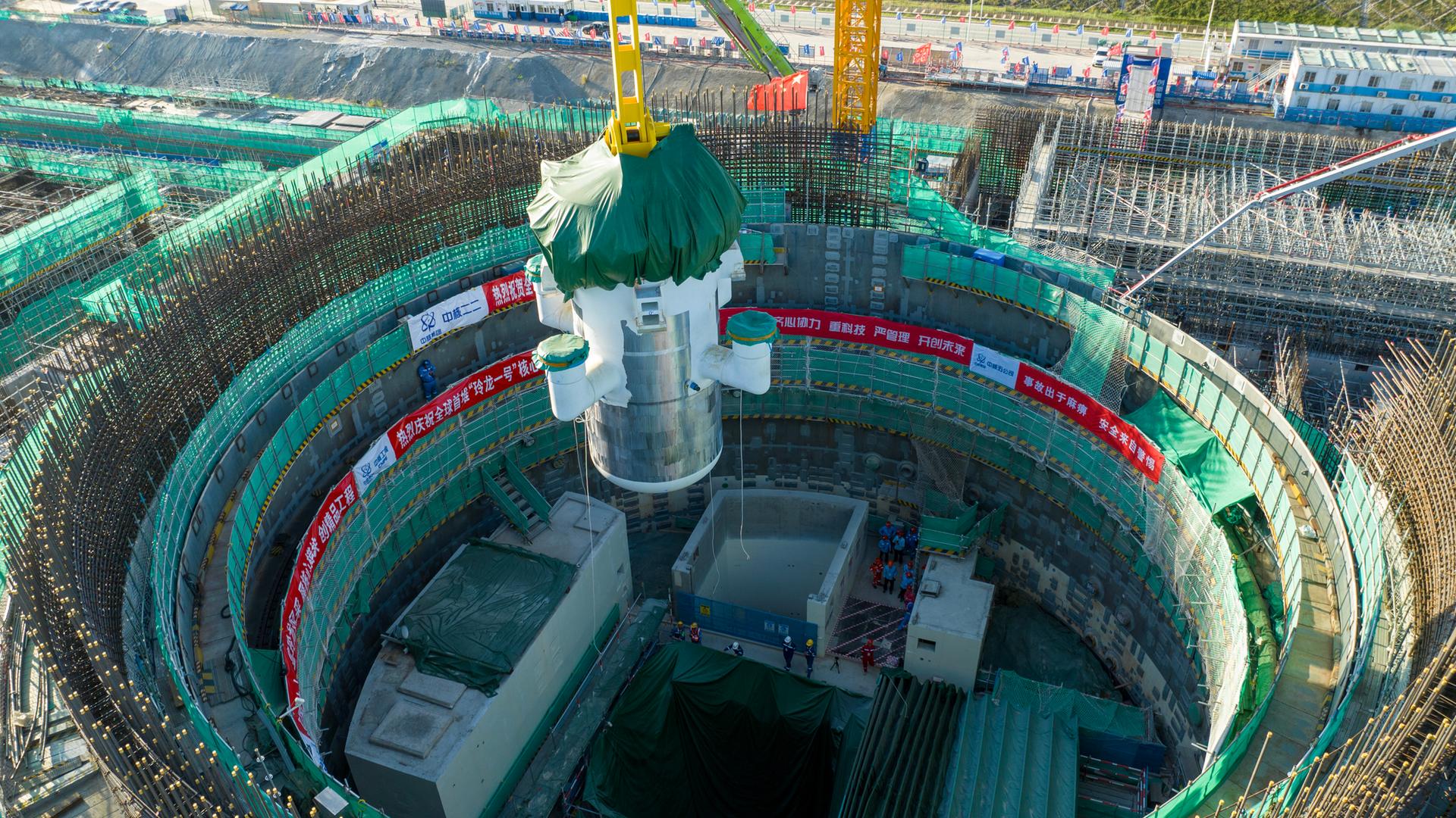 Das Foto zeigt eine große Industriehalle oder Montageanlage. In der Mitte befindet sich ein massives, zylindrisches Bauteil eines kleinen modularen Reaktors, das von einem gelben Stahlgerüst umgeben ist.