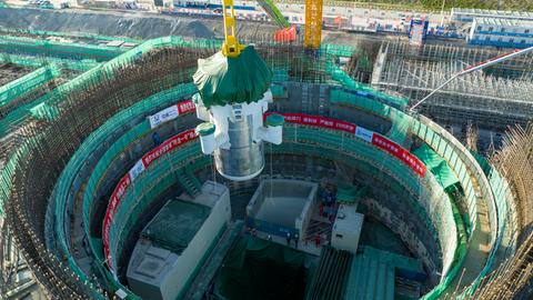 Das Foto zeigt eine große Industriehalle oder Montageanlage. In der Mitte befindet sich ein massives, zylindrisches Bauteil eines kleinen modularen Reaktors, das von einem gelben Stahlgerüst umgeben ist.
