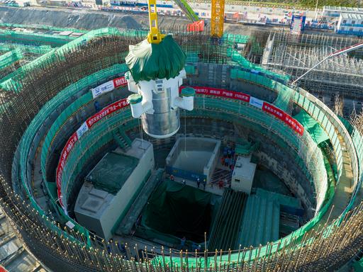 Das Foto zeigt eine große Industriehalle oder Montageanlage. In der Mitte befindet sich ein massives, zylindrisches Bauteil eines kleinen modularen Reaktors, das von einem gelben Stahlgerüst umgeben ist.