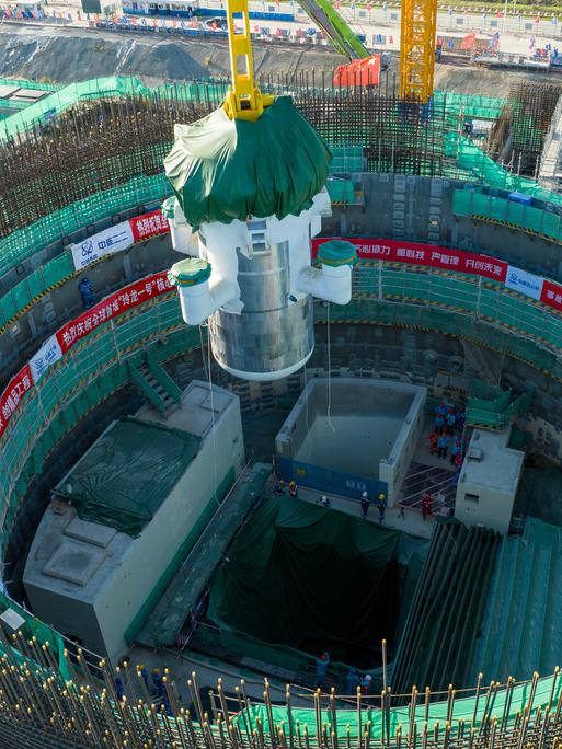 Das Foto zeigt eine große Industriehalle oder Montageanlage. In der Mitte befindet sich ein massives, zylindrisches Bauteil eines kleinen modularen Reaktors, das von einem gelben Stahlgerüst umgeben ist.