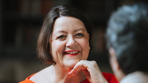 Die Gründerin des Vereins "Nestwärme", Petra Moske, schaut zu einer Gesprächspartnerin. Sie trägt ein rotes Oberteil und hat ihre linke Hand gegen ihr Kinn gelegt.