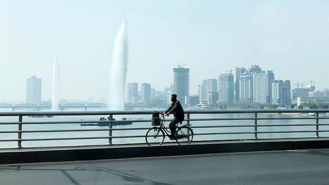 Ein Fahrradfahrer fährt über eine Brücke über den Taedong-Fluss in Pjöngjang. Im Hintergrund sind Hochhäuser zu sehen.
