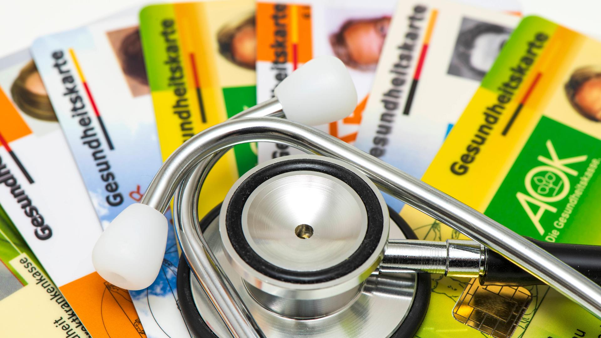 Ein Stethoskop liegt auf Gesundheitskarten von verschiedenen Krankenkassen als Symbolbild für steigende Krankenkassenbeiträge und notwendige Reformen im Gesundheitssystem