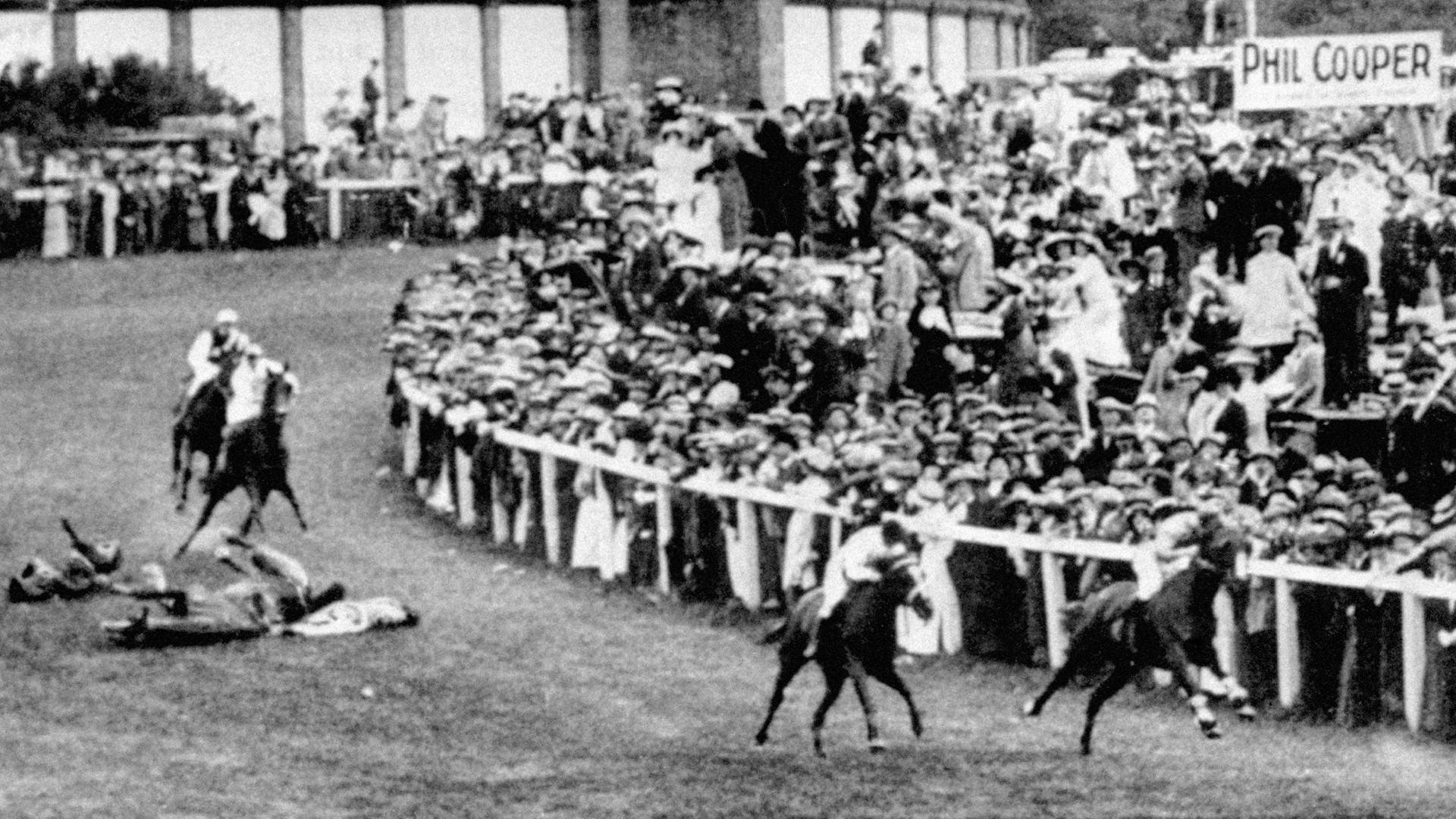 Historisches Foto vom Epsom Derby 1913, mit Pferden und Zuschauern sowie gestürzten Tieren und einem Mensch auf dem Boden der Rennbahn
