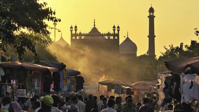 Menschenmenge auf einem belebten Markt bei Sonnenuntergang, im Hintergrund sind historische Gebäude sichtbar.