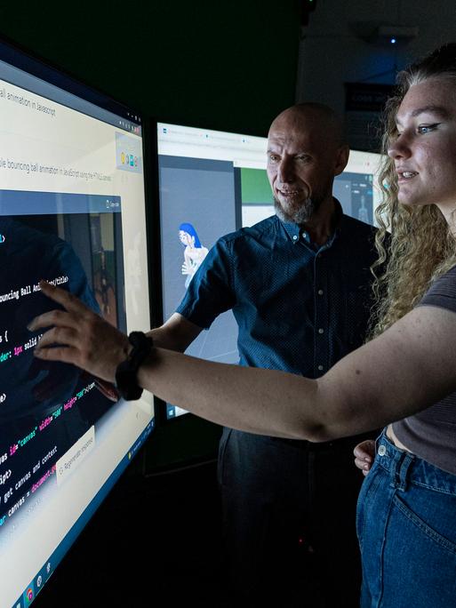 Studierende stehen mit ihrem Professor vor einem großen Bildschirm und nutzen eine Künstliche Intelligenz