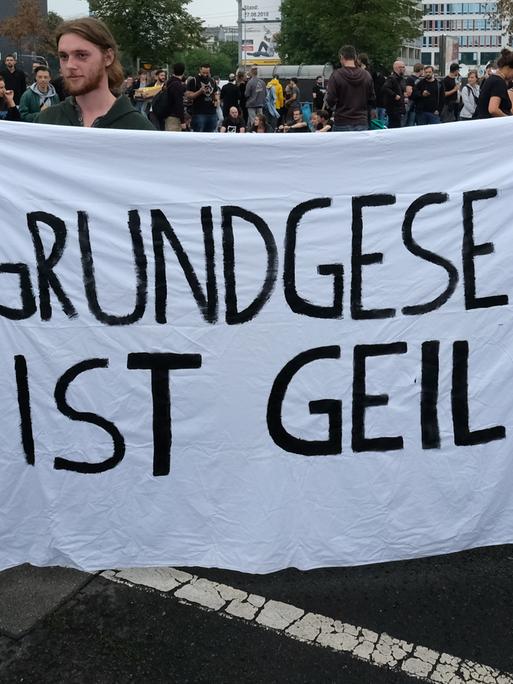 Zwei Personen halten am Rande eines Konzerts in Chemnitz ein Banner in der Hand mit der Aufschrift „Grundgesetz ist geil!“. 