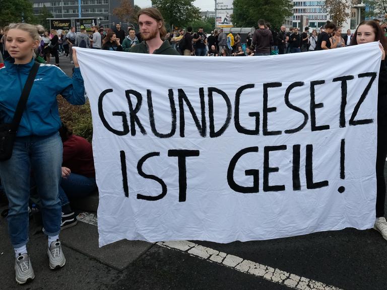 Zwei Personen halten am Rande eines Konzerts in Chemnitz ein Banner in der Hand mit der Aufschrift „Grundgesetz ist geil!“. 