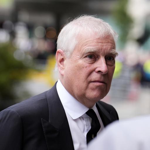 Prinz Andrew in einer Nahaufnahme im Freien. Er trägt einen schwarzen Anzug mit weißem Hemd und schwarzer Krawatte.