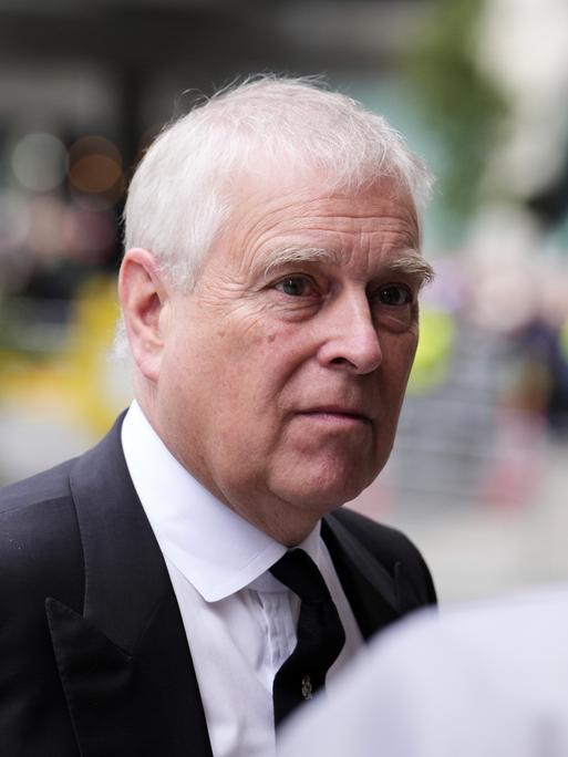 Prinz Andrew in einer Nahaufnahme im Freien. Er trägt einen schwarzen Anzug mit weißem Hemd und schwarzer Krawatte.