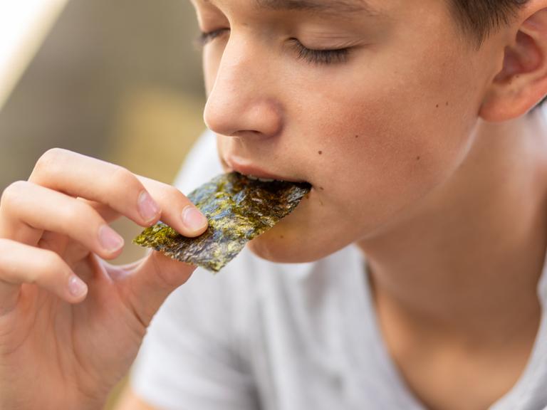 Ein junger Mann schiebt sich einen Algenbrotchip in den Mund Ein junger Mann schiebt sich einen Algenbrotchip in den Mund