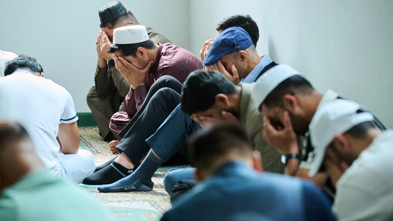 Muslimische Männer beten in der Moschee. Mehrere Männer halten zum Gebet das Gesicht verdeckt und sitzen auf dem Boden. 