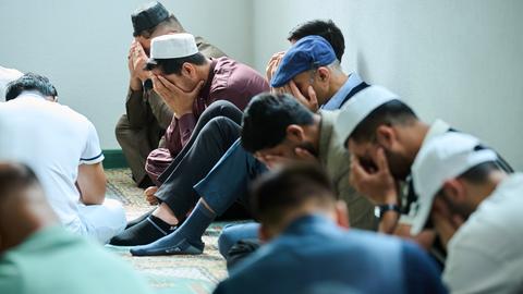 Muslimische Männer beten in der Moschee. Mehrere Männer halten zum Gebet das Gesicht verdeckt und sitzen auf dem Boden. 