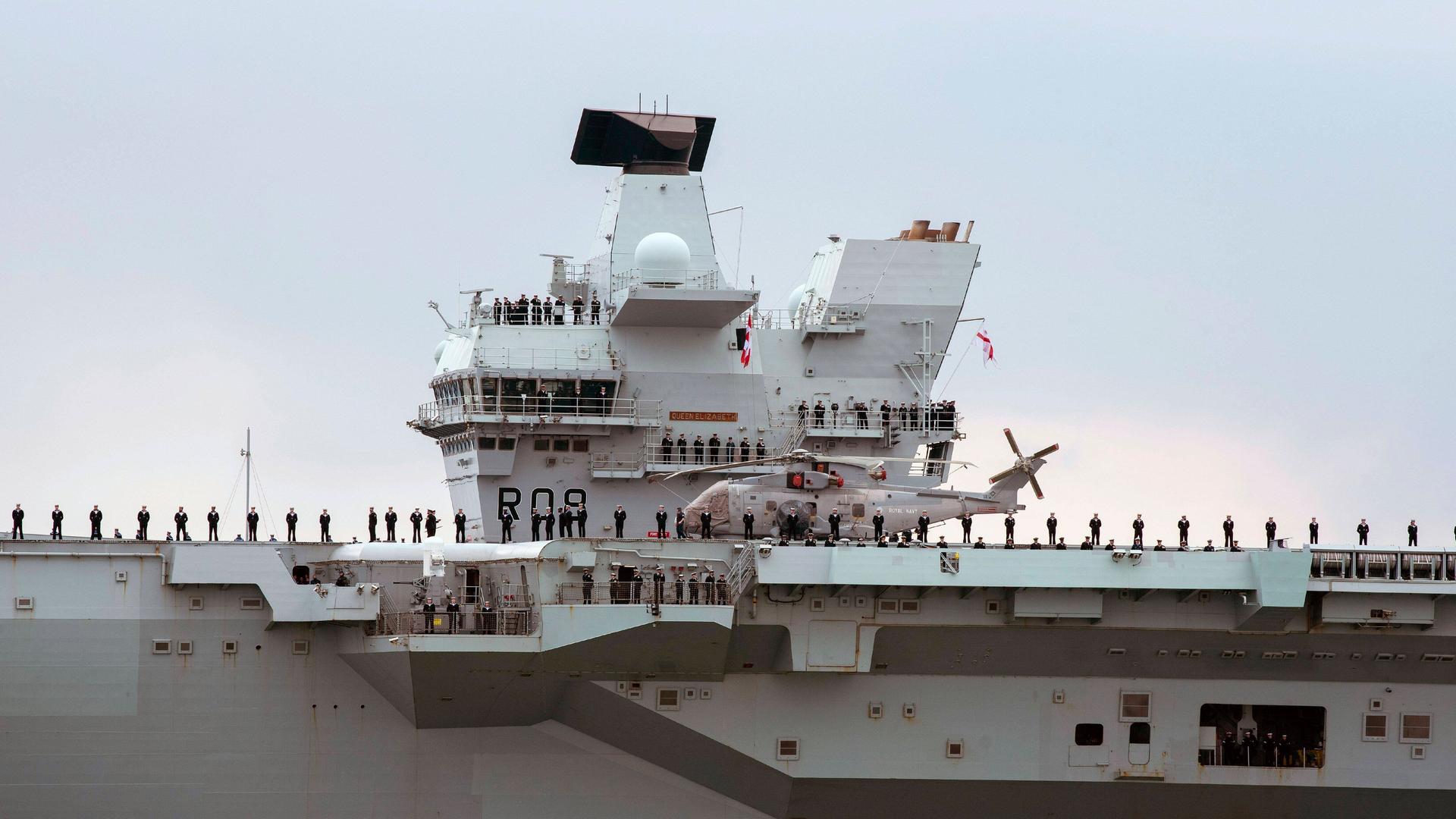 Der Blick auf das Hauptdeck eines britischen Kriegsschiffes, Soldaten und ein Hubschrauber stehen auf dem obersten Deck.