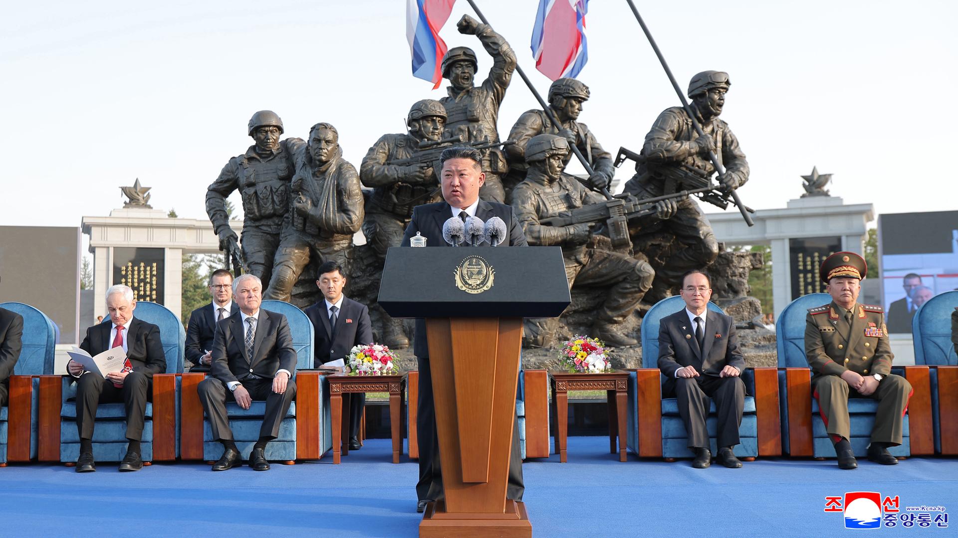 Kim Jong Un hält einer Rede während der Einweihungszeremonie des Museums für militärische Auslandsoperationen und Kampferfolge in Pjöngjang. Hinter ihm sitzen Generäle, hinter ihnen ist ein Denkmal mit mehreren Soldaten. 